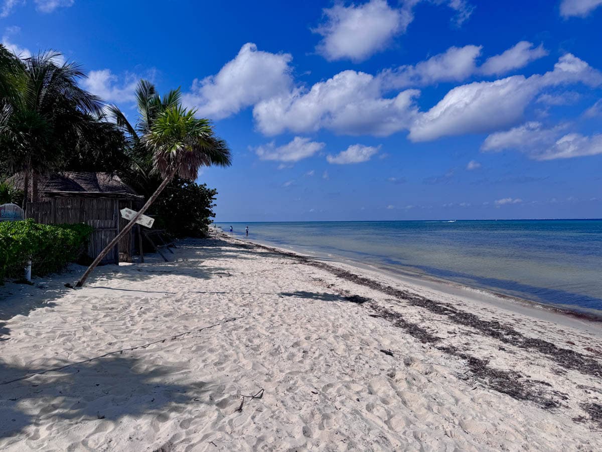 Beach with white sand and blue sky with a few white clouds.