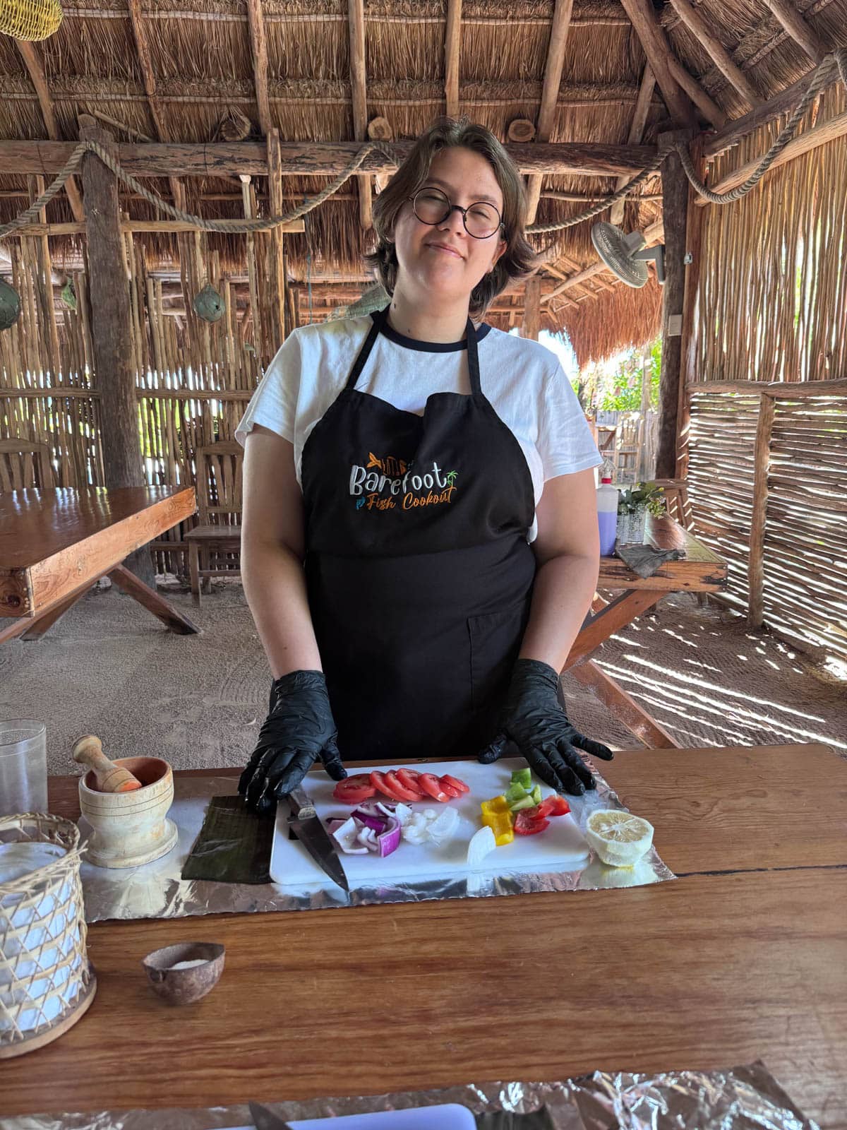 Woman with apron on in front of cutting board with vegetables.