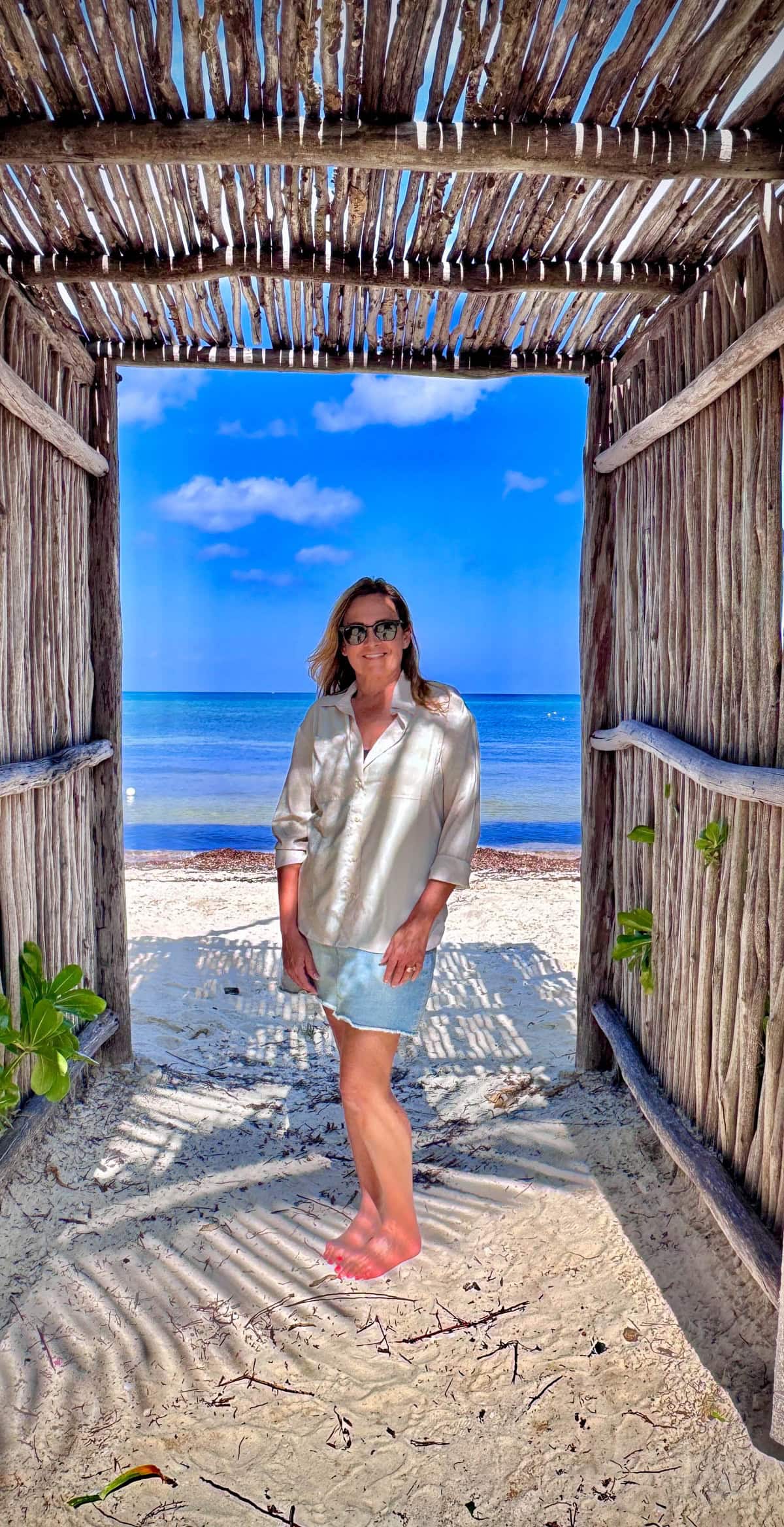 Woman standing in doorway with beach and sky in background.