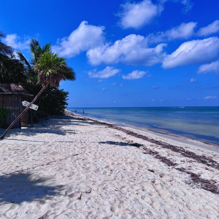 Beach with white sand and blue sky with a few white clouds.