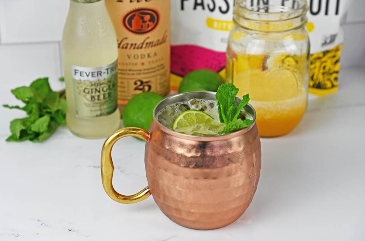 Drink with a lime and mint in a mule copper cup with ingredients in the background.