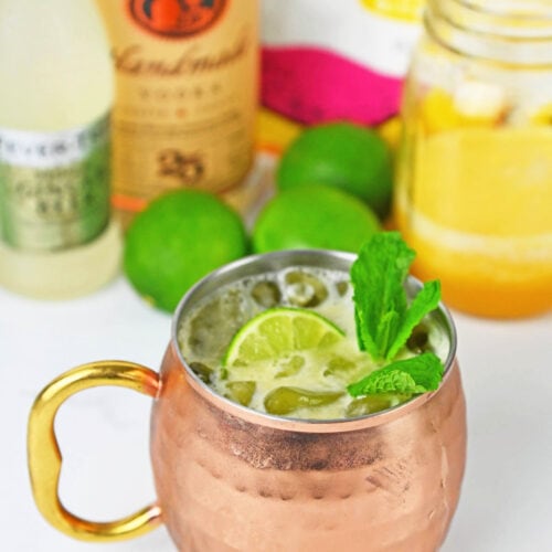 Drink with a lime and mint in a mule copper cup with ingredients in the background.