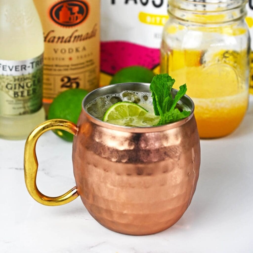 Drink with a lime and mint in a mule copper cup with ingredients in the background.