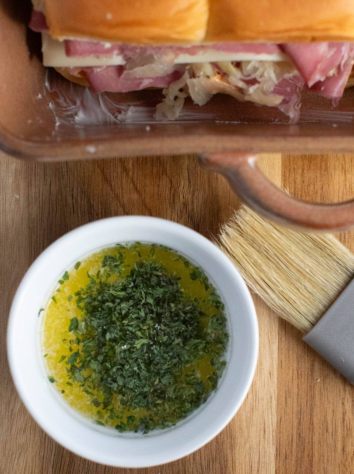 Sauce for slider sandwiches with basting brush and baking dish of sliders in background.