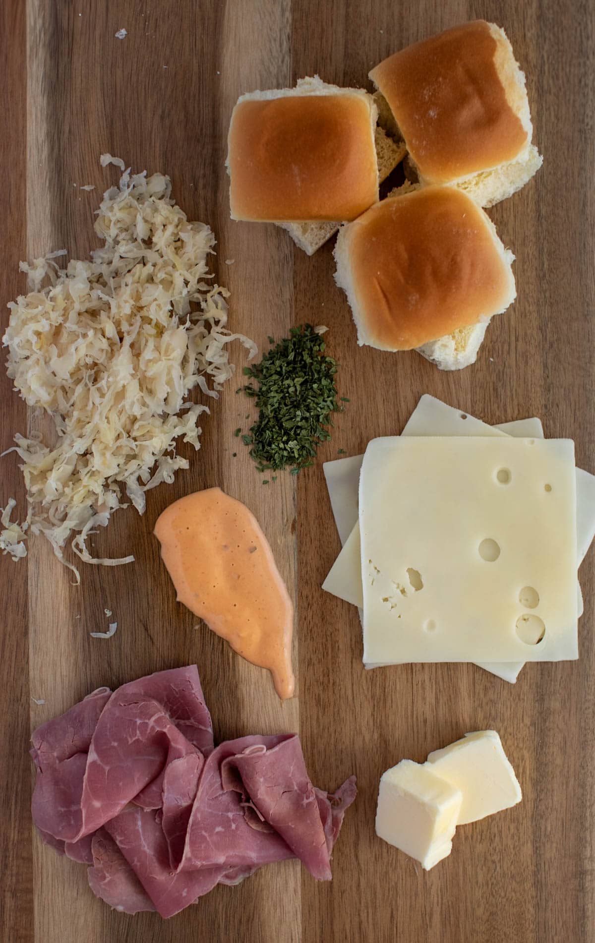 Ingredients to make Reuben sliders on a wood cutting board.