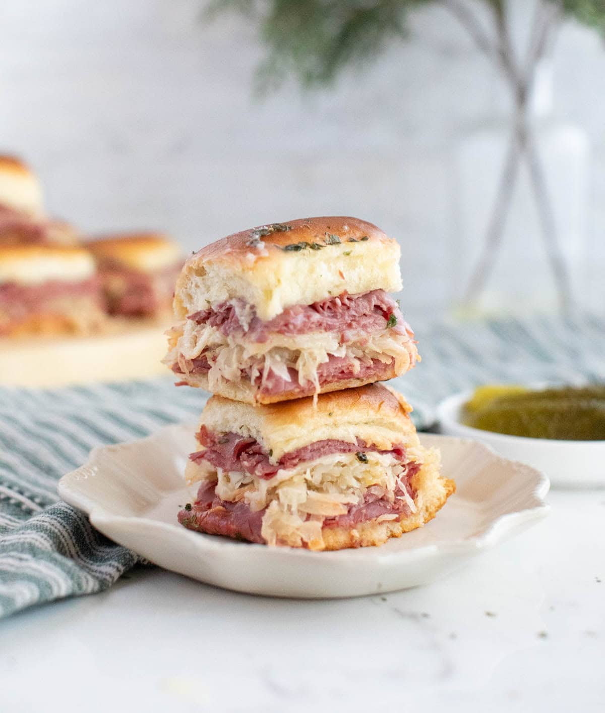 Reuben sandwiches stacked on a white plate with a striped dish towl.