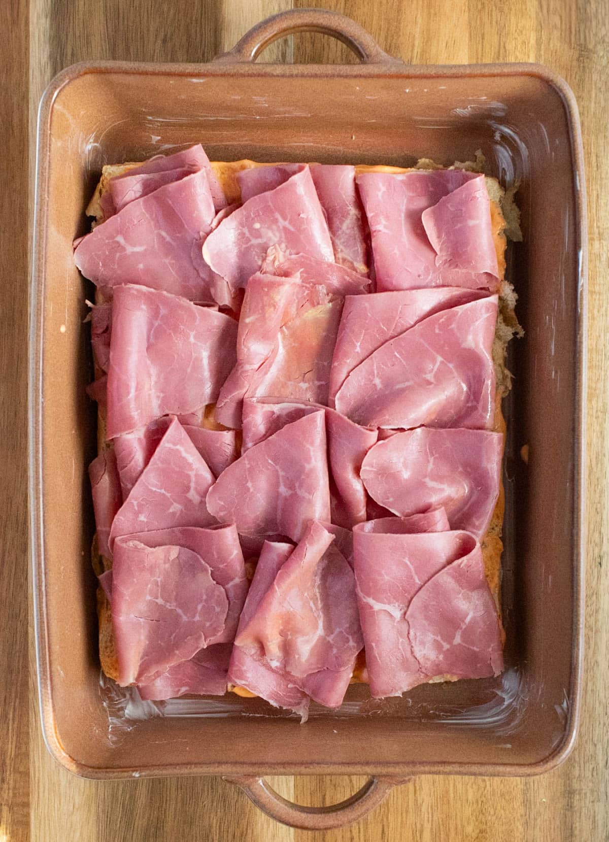 Sliced corned beef on bottoms of rolls in a baking dish.