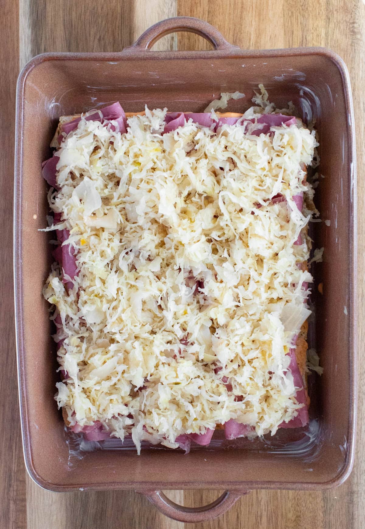 Sliced corned beef and sauerkraut on bottoms of rolls in a baking dish.