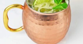 Drink with a lime and mint in a mule copper cup with ingredients in the background.