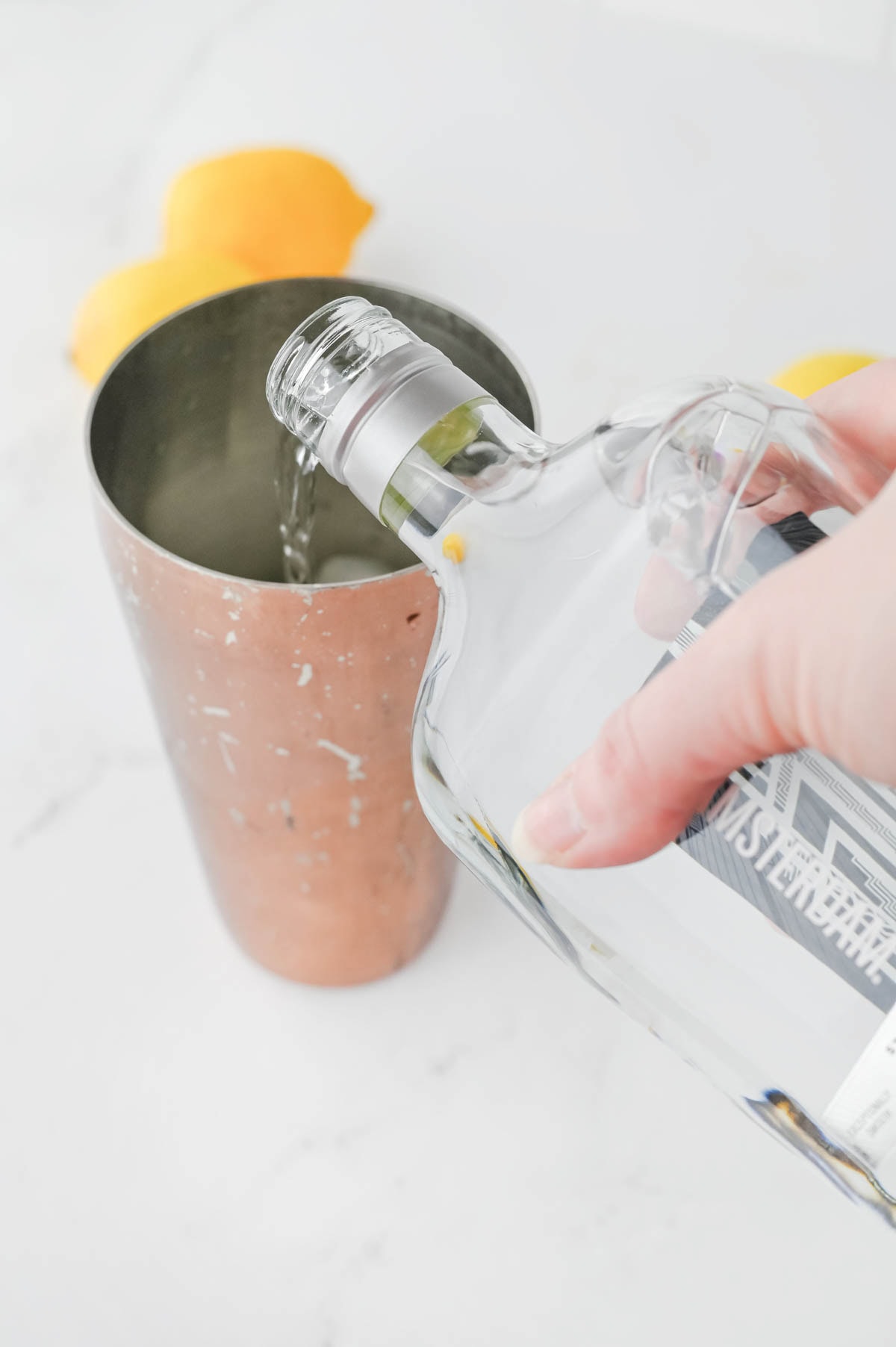 Pouring white liquid into a cocktail shaker with two lemons in background.