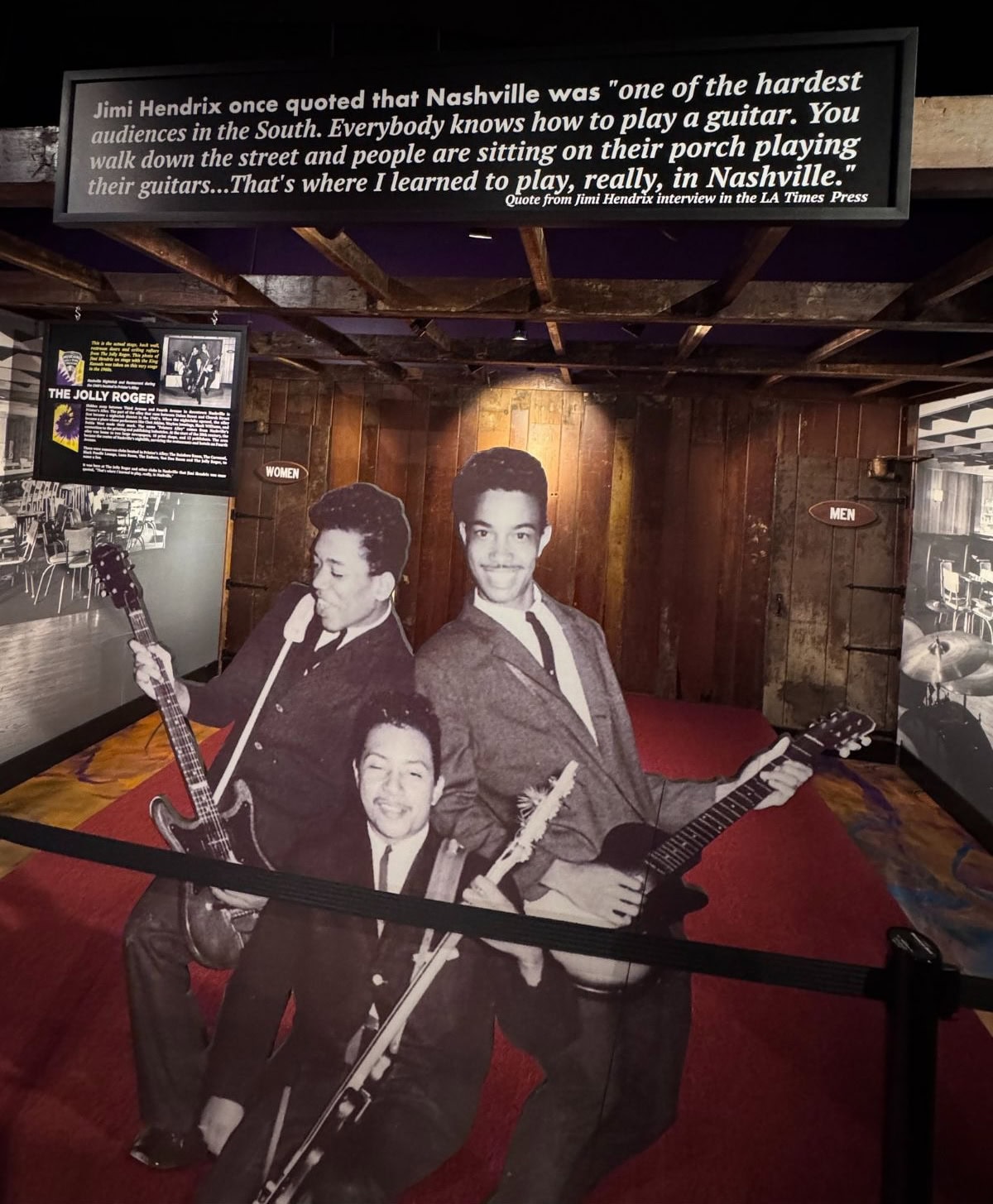 Cutouts of 3 men playing guitars in a museum.