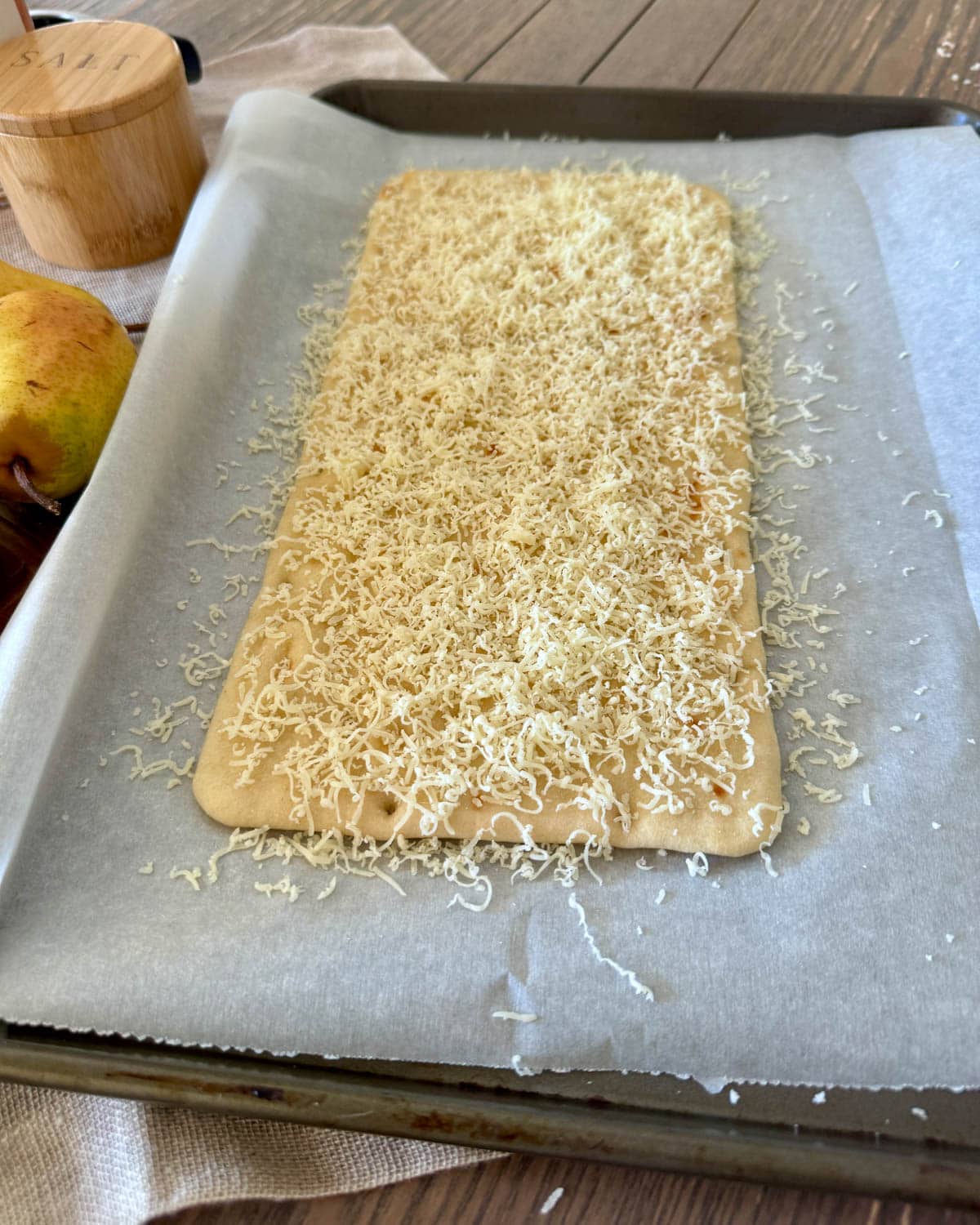 Flatbread with shredded cheese on parchment paper on baking sheet.