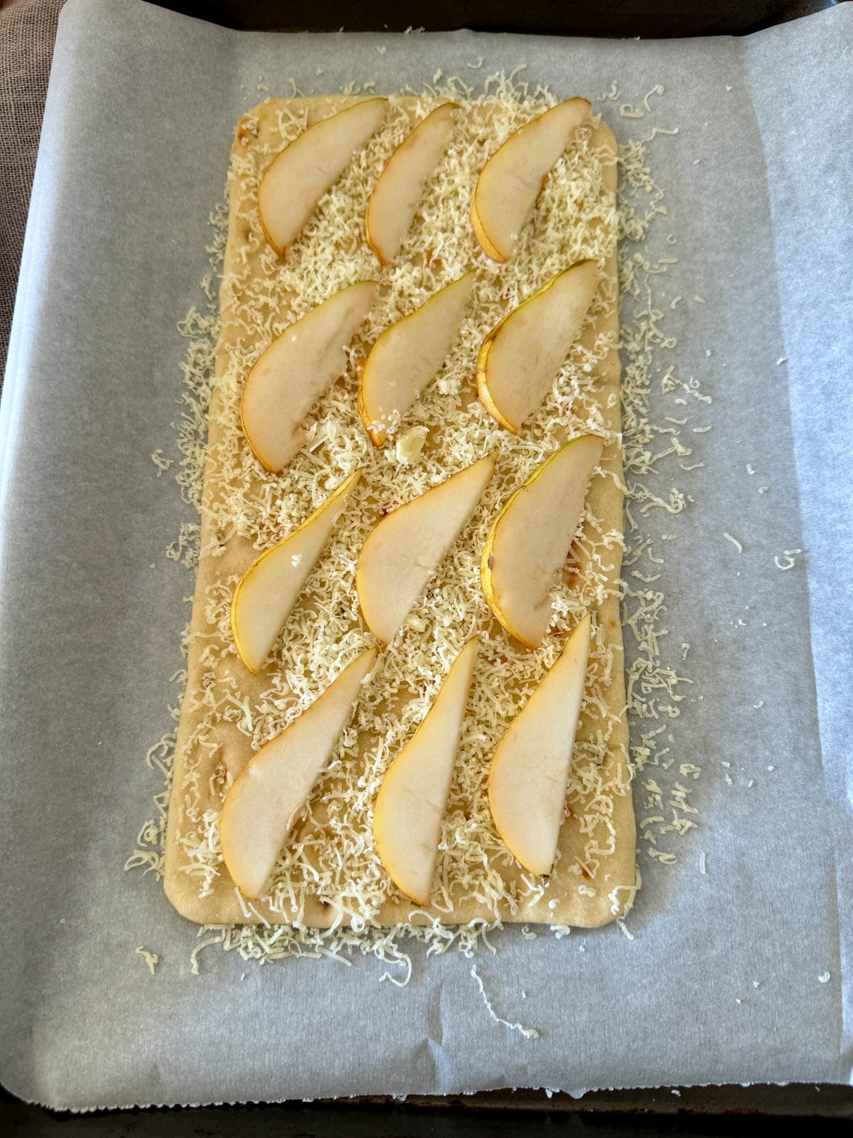Flatbread with cheese and sliced pear on parchment.
