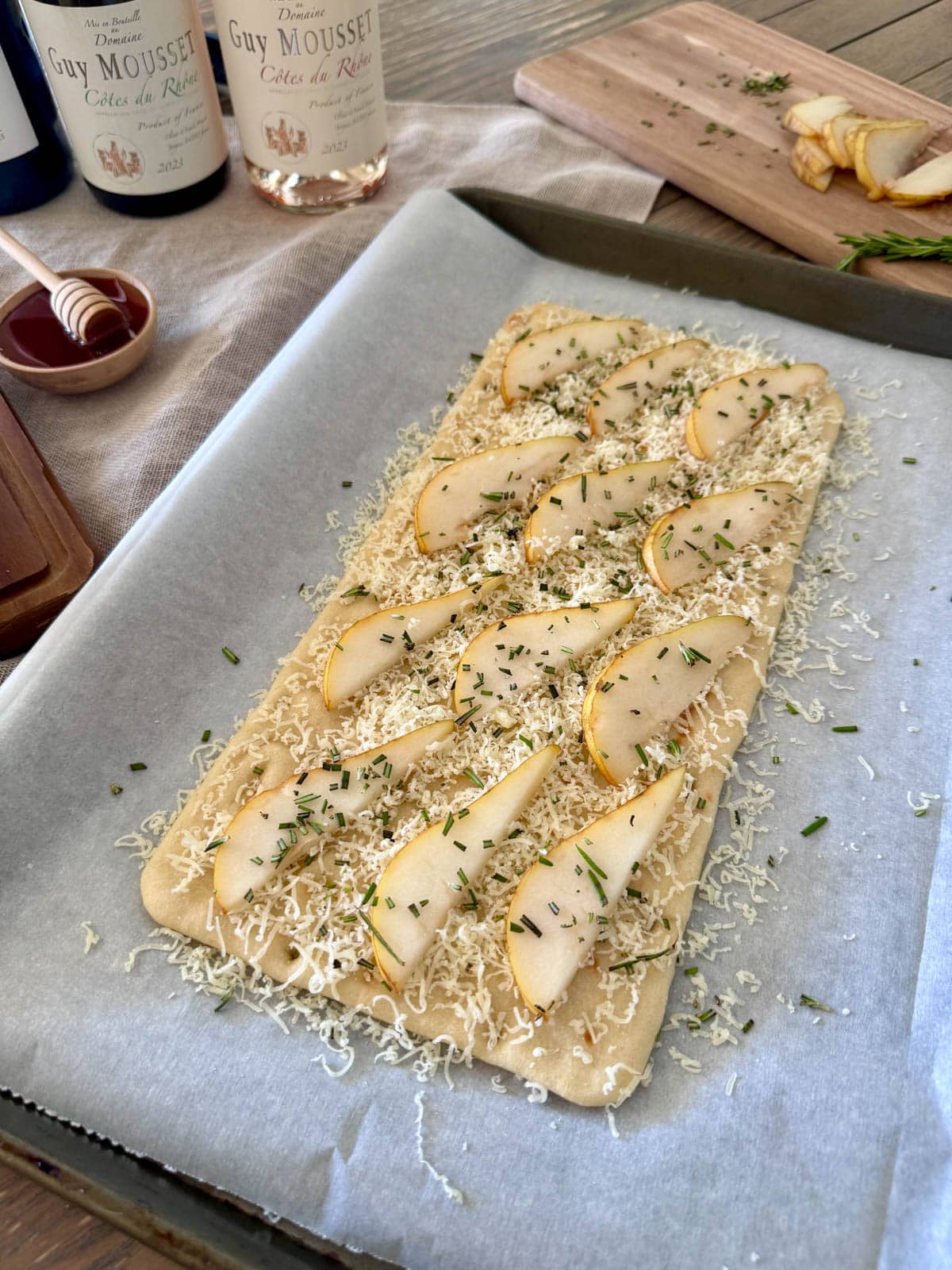 Flatbread with cheese, sliced pear, and rosemary on parchment.