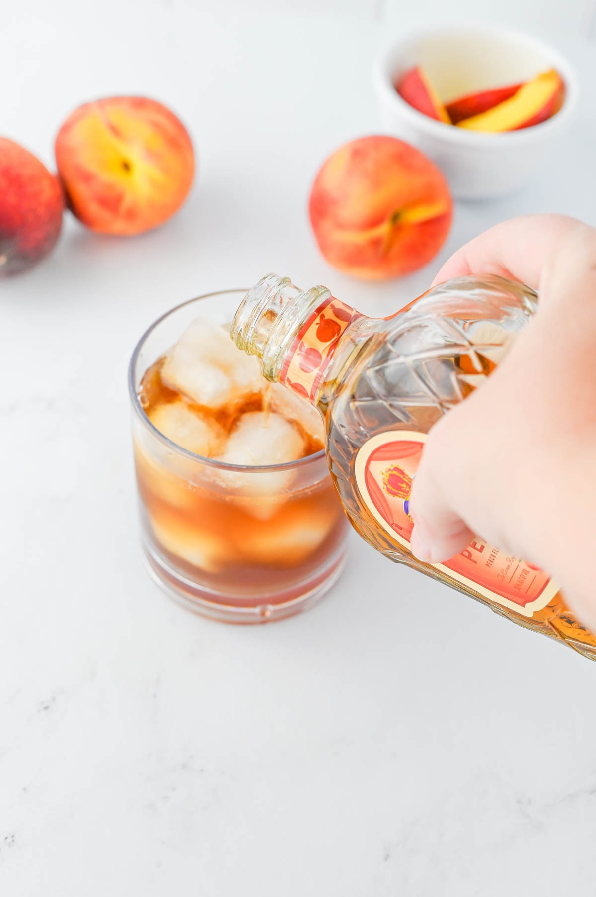Pouring whiskey into a glass of iced tea.