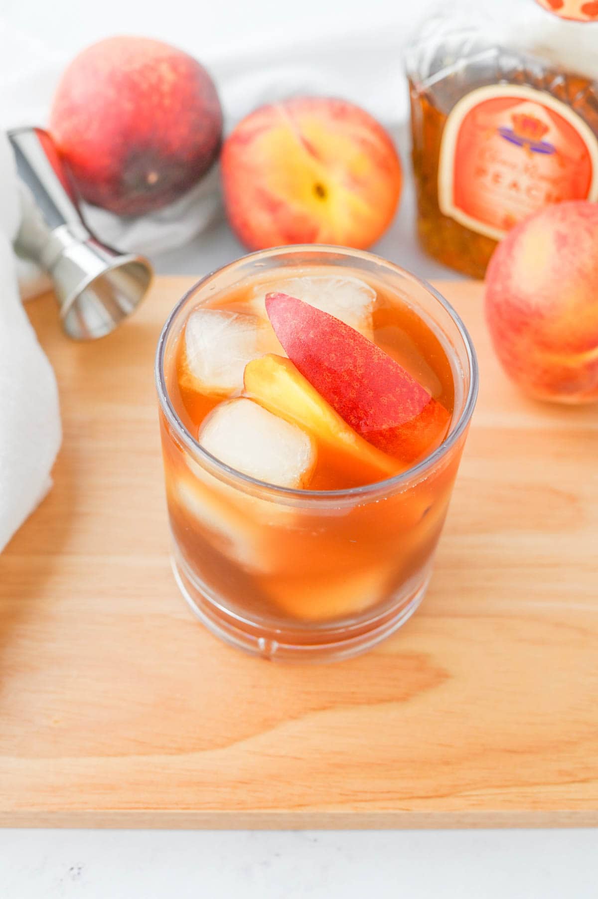 A glass of peach tea with a slice of peach on a cutting board.