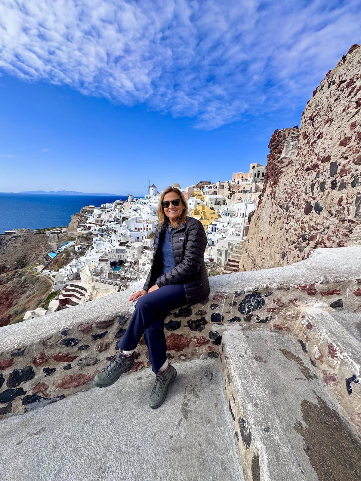 Woman sitting on a wall in Santorini Greece with white-washed houses in the background.