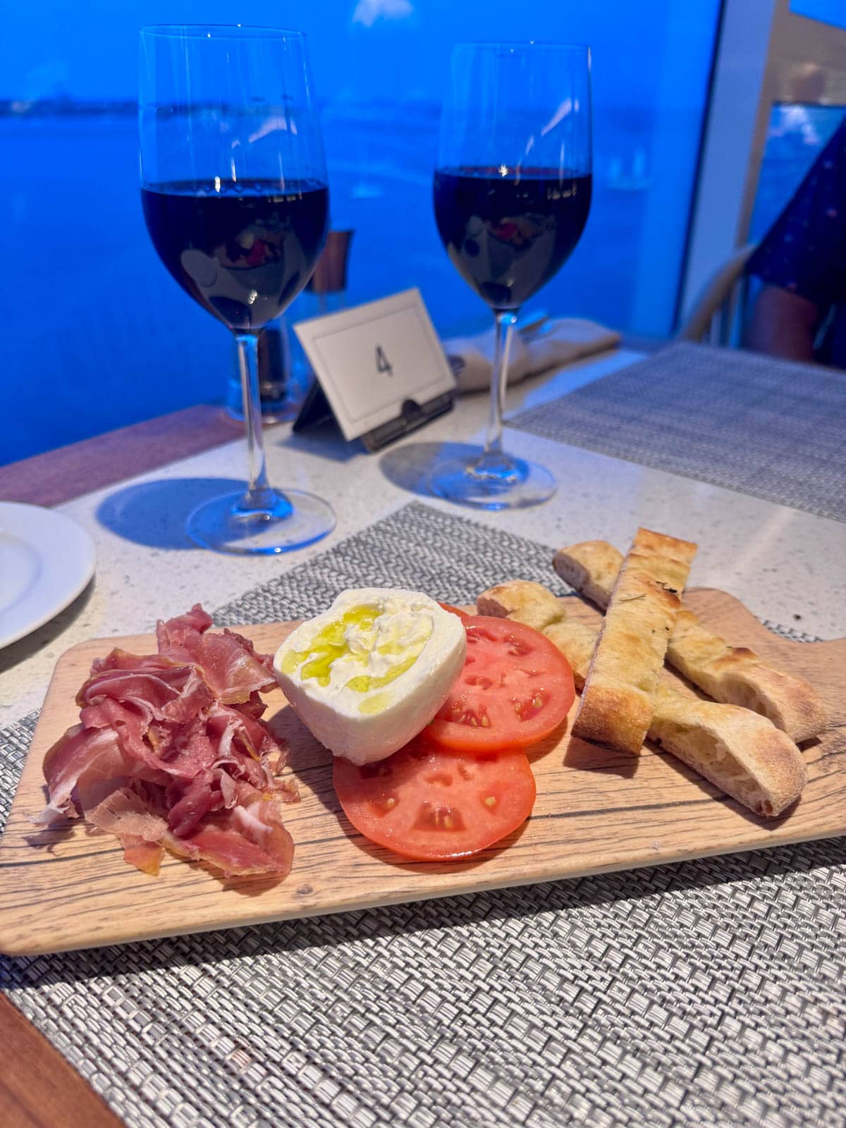 Wood board with focaccia bread, tomatoes, bursata cheese, and proscuitto.