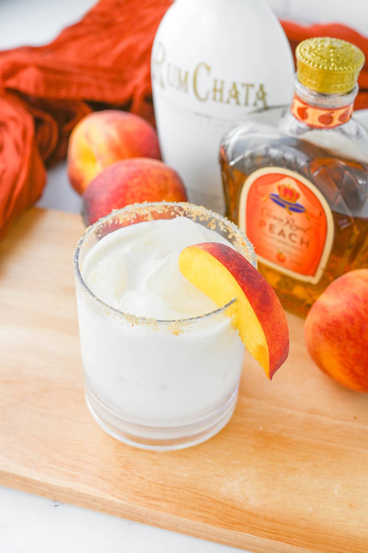 White liquid in a glass with sugar rim on a wood board with peaches and Crown Royal bottle in background.