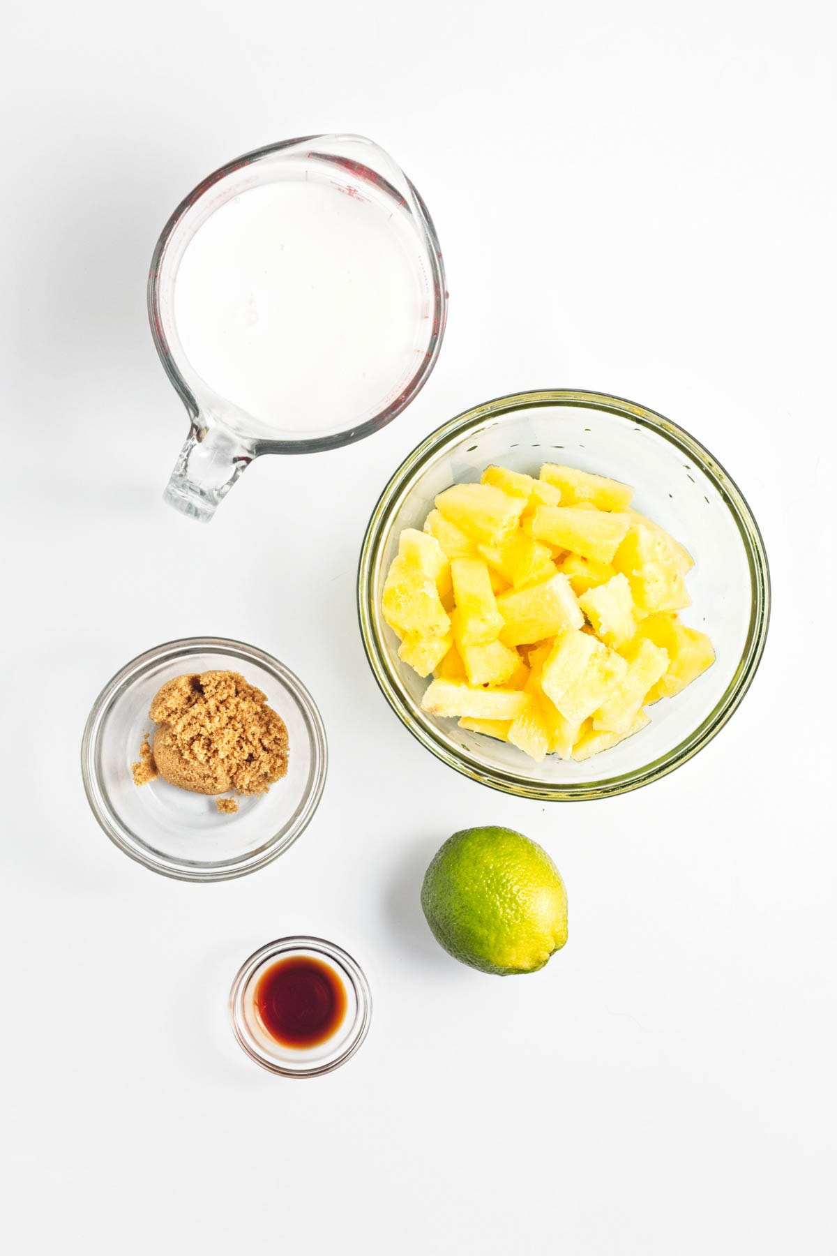 Pineapple, brown sugar, lime, vanilla, and coconut milk in glass bowls.