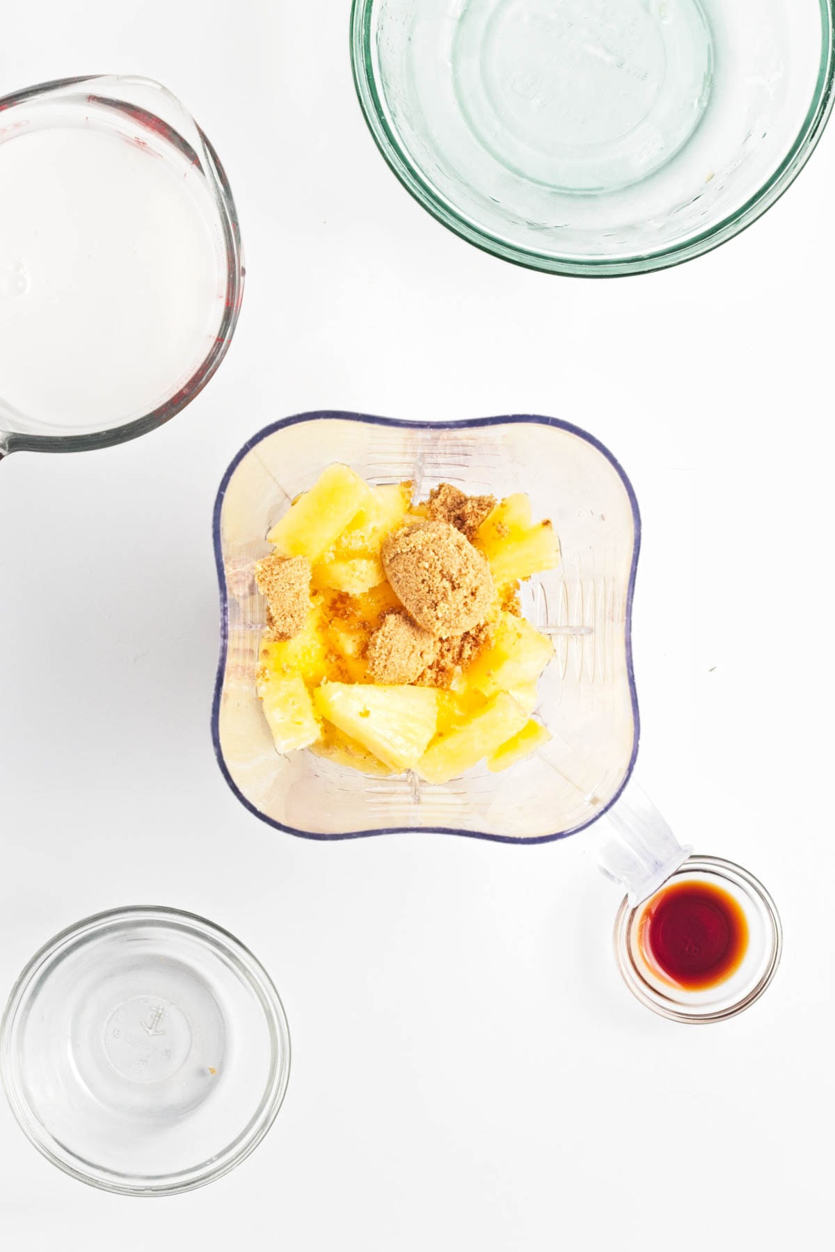 Pineapple and brown sugar in a blender with small bowl of vanilla to side.