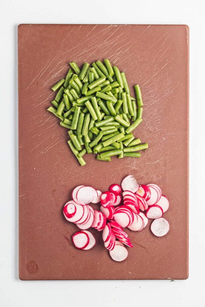 Green beans and radishes on a cutting board.