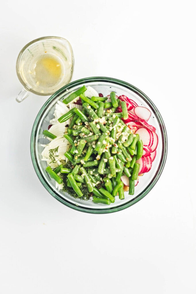 Green beans over radishes and onions with dressing poured over top.