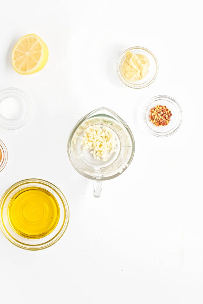 Small glass bowls with onion, garlic, seasoning, olive oil, and a lemon half to the side.