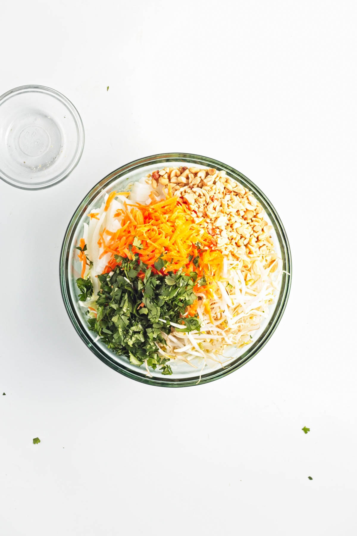 A glass bowl of vegetables with peanuts and an empty glass bowl on side.