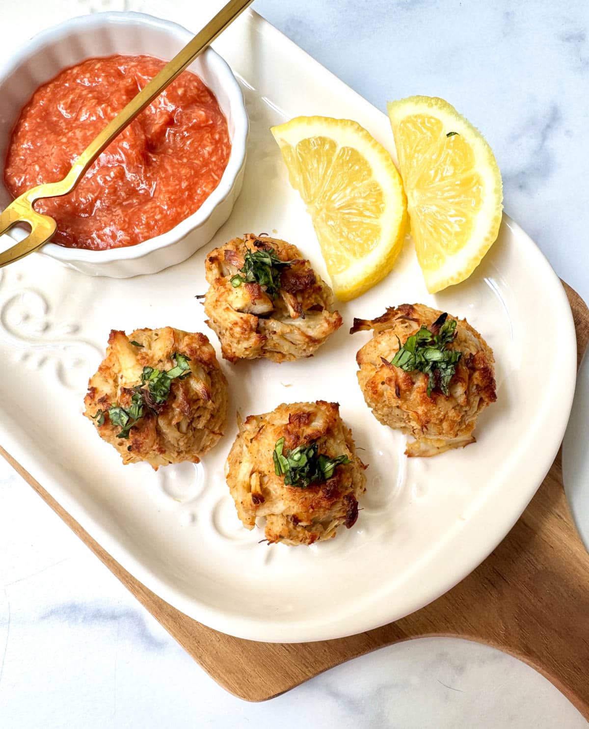 Crab balls on white plate with lemon slices and cocktail sauce in a white bowl with a gold fork.