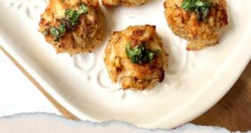 Crab balls on white plate with lemon slices and cocktail sauce in a white bowl with a gold fork Pinterest graphic.
