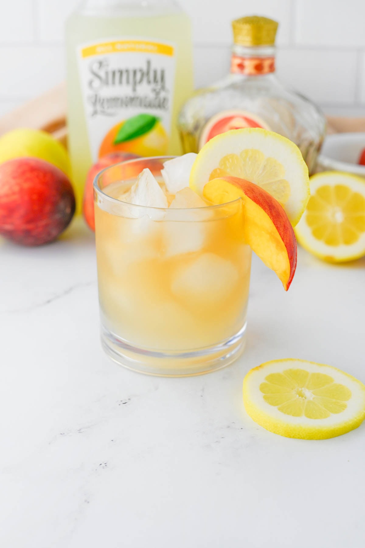 Golden colored cocktail with bottle of lemonade and bottle of Crown Royal in background with peaches and lemons.