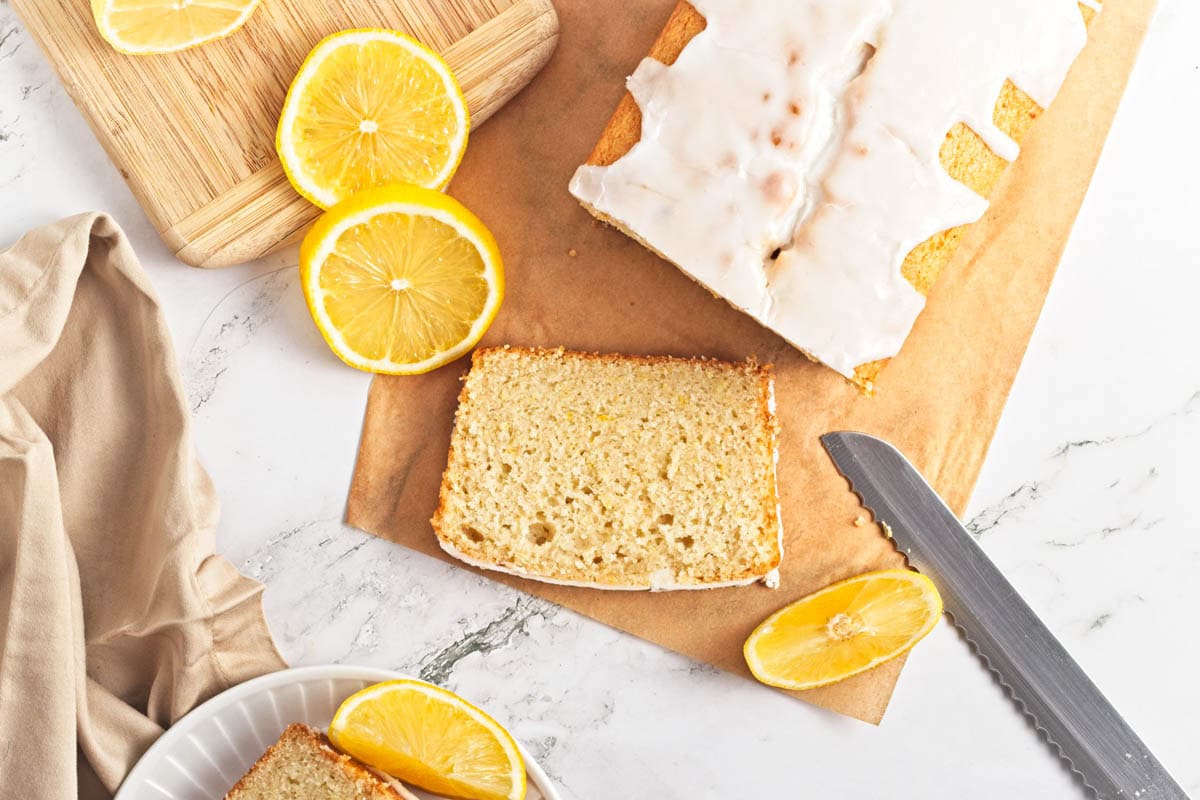 Lemon loaf cake on parchment paper with lemon pieces scattered on wood cutting board.