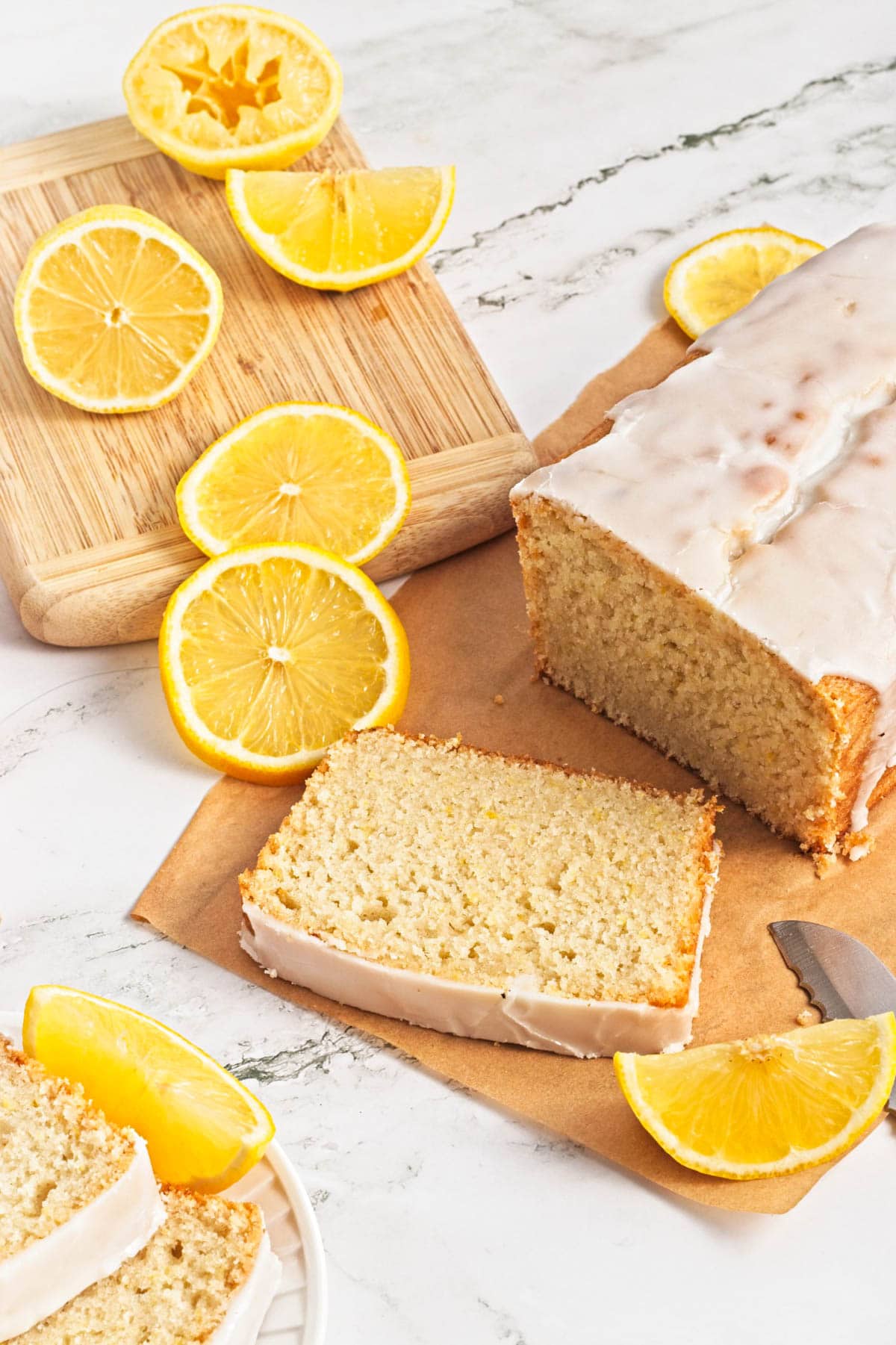 Lemon loaf cake on parchment paper with lemon pieces scattered on wood cutting board.