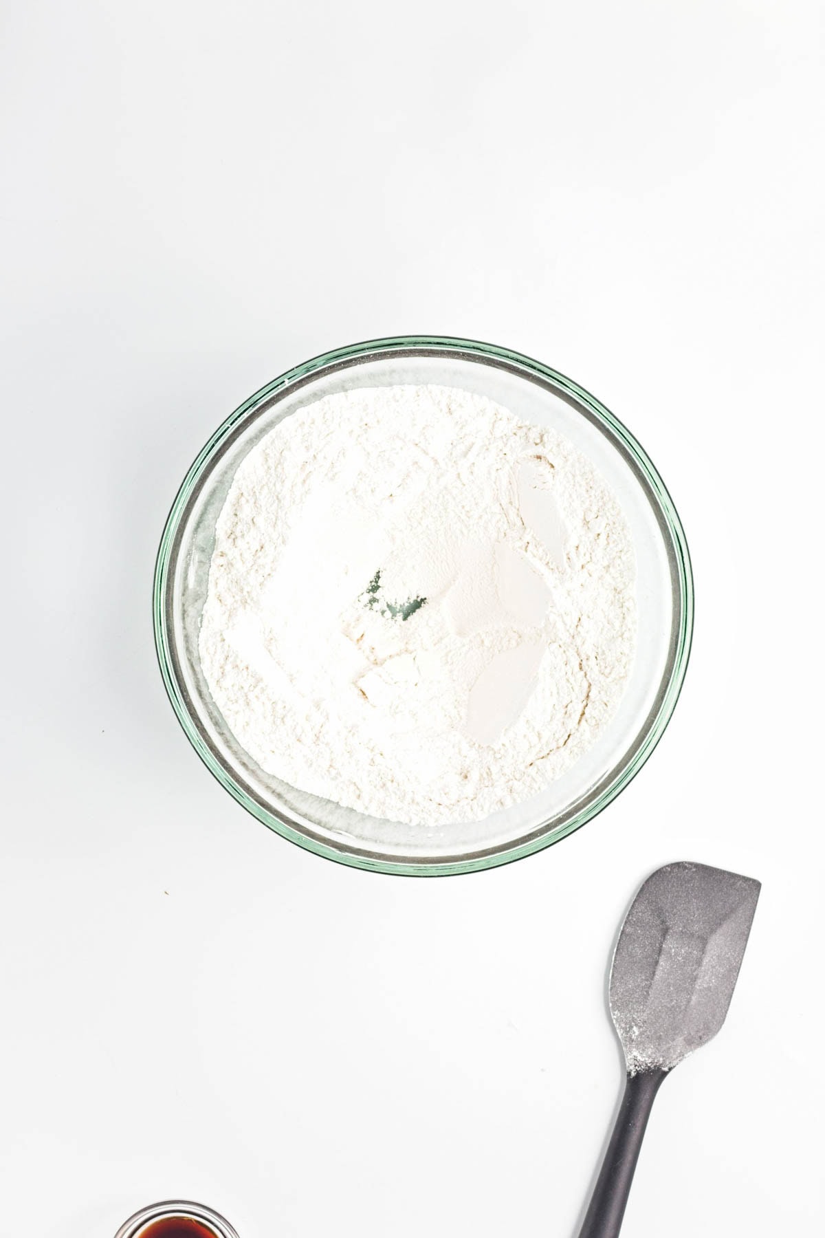 Glass bowl with dry ingredients and well in center with spatula to side.