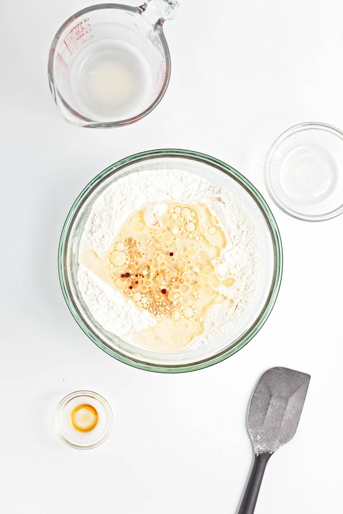 Flour mixture in glass bowl with milk, vanilla, and oil in well in center.