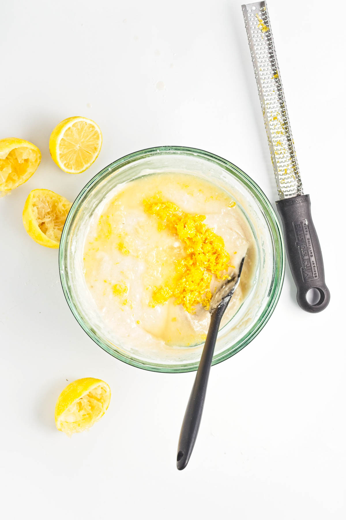Lemon juice and zest mixed with milk in glass bowl with spatula and lemon zest tool.