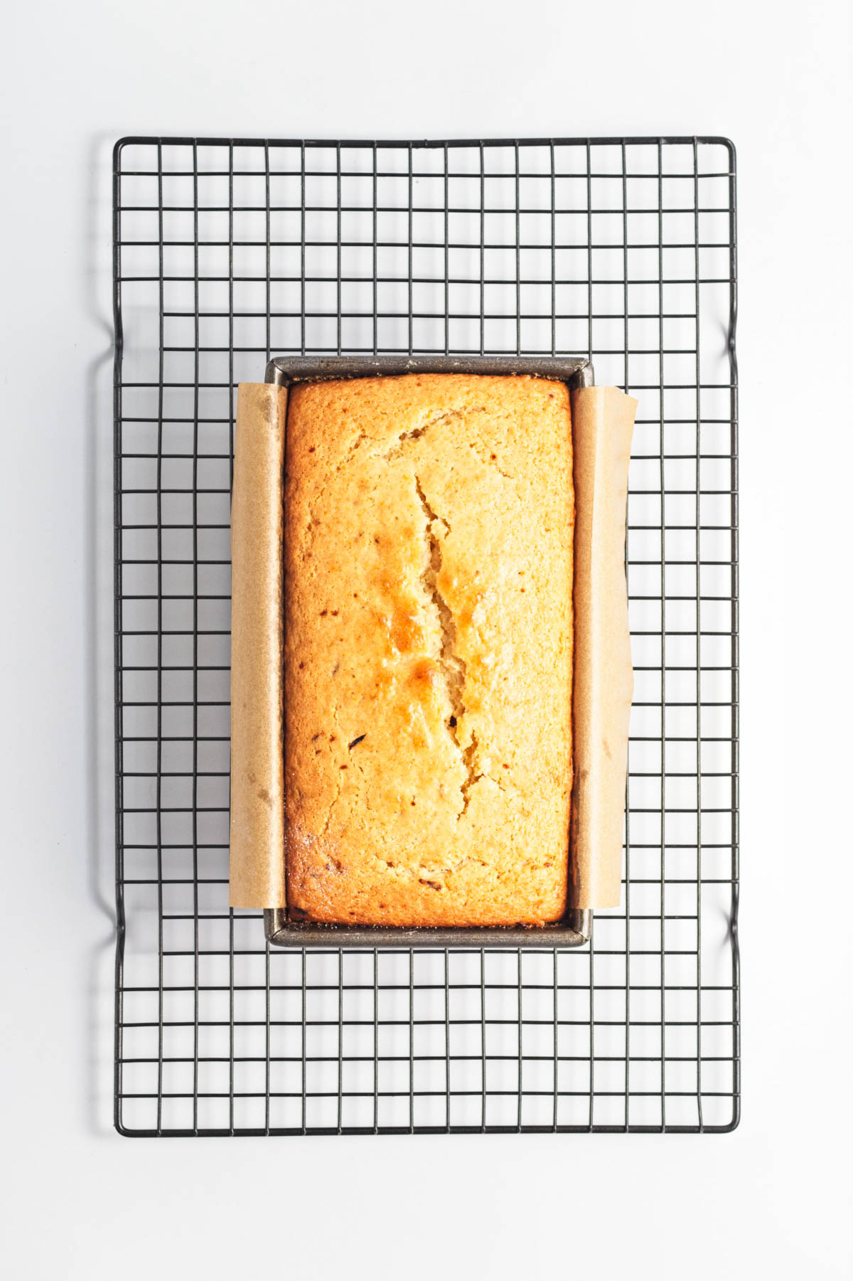 Baked cake in loaf pan over parchment paper over a wire rack.