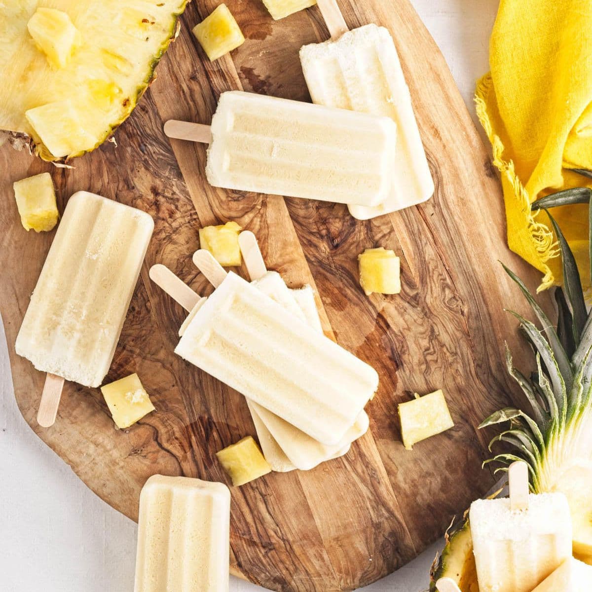 Yellow popsicles on a wood board with fresh pineapple in background.