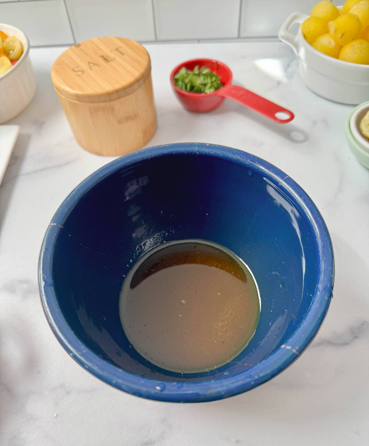 Blue bowl with salad dressing and a salt container and cup of mint above.