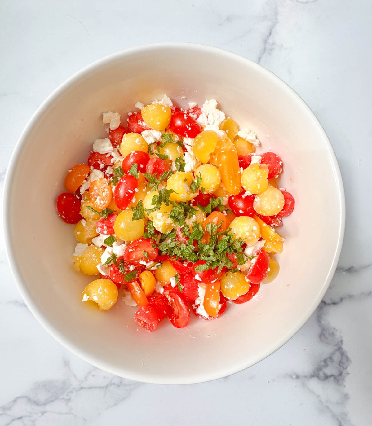 White bowl with watermelon and tomatoes and feta cheese and mint.