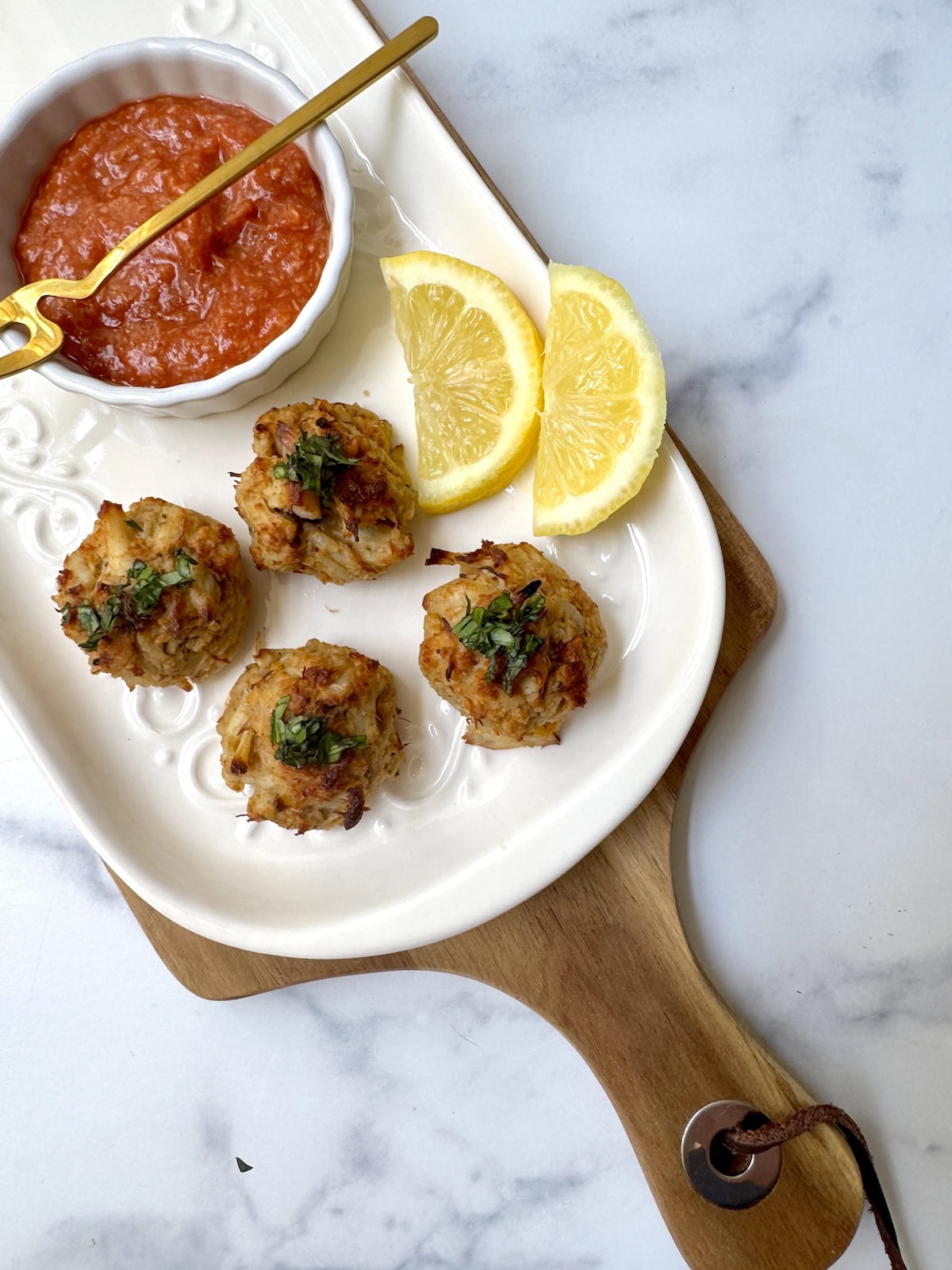 Crab balls on white plate with lemon slices and a bowl of cocktail sauce.