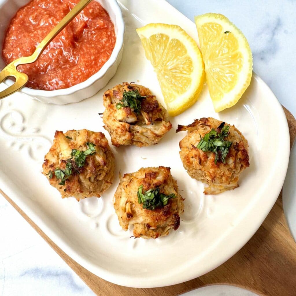 Crab balls on white plate with lemon slices and cocktail sauce in a white bowl with a gold fork.