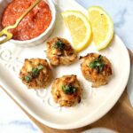 Crab balls on white plate with lemon slices and cocktail sauce in a white bowl with a gold fork.