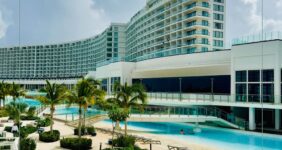 Hotel with swimming pool in front and longe chairs in front of pool.