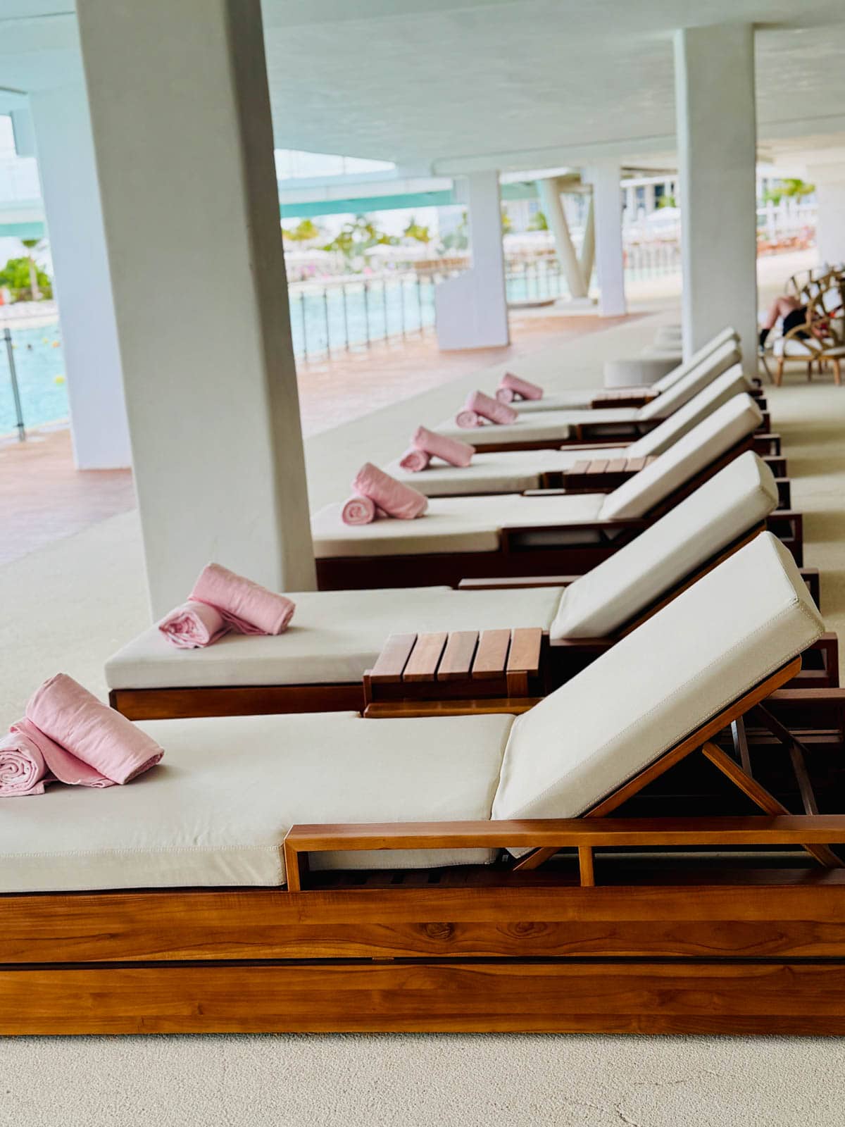 Lounge chairs with pink towels rolled up at bottom at swimming pool.