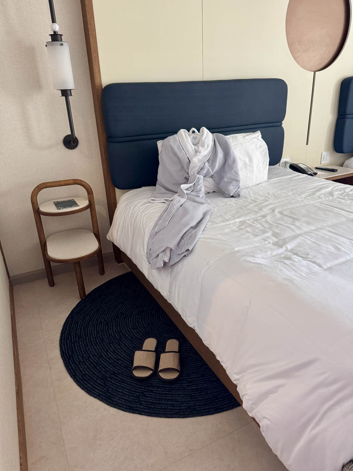 Room in hotel with a robe on bed and slippers on rug by bed.
