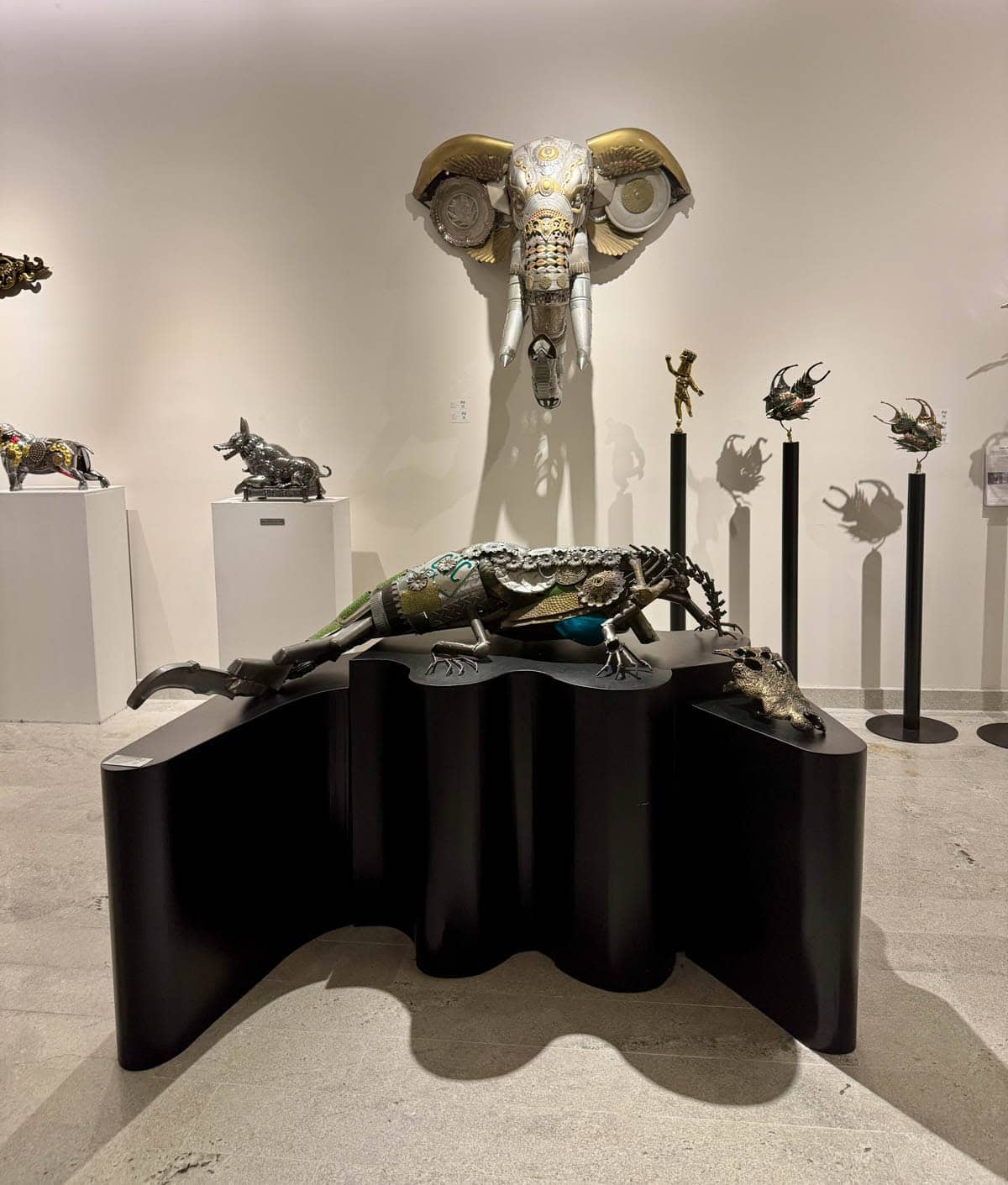 Art gallery with elephant head sculpture on wall and alligator sculpture on table.