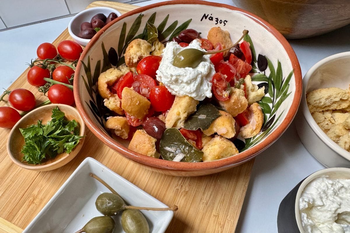 Salad with tomatoes, parsley, croutons, capers, and whipped feta cheese in a bowl with small bowls of ingredients to the side.