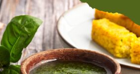 Basil olive oil dipping sauce in a small wooden bowl with fresh basil and bread sticks in the background.
